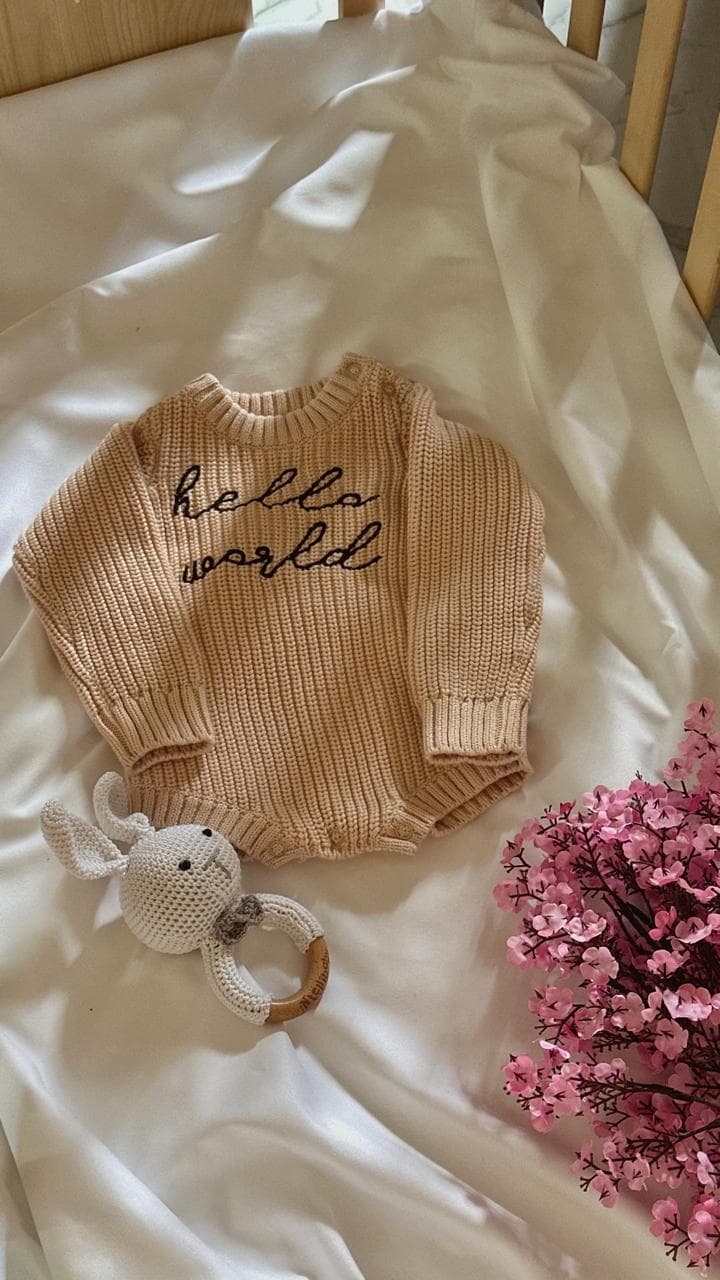 Hello World knitted romper with elephant rattle and pink flowers in crib