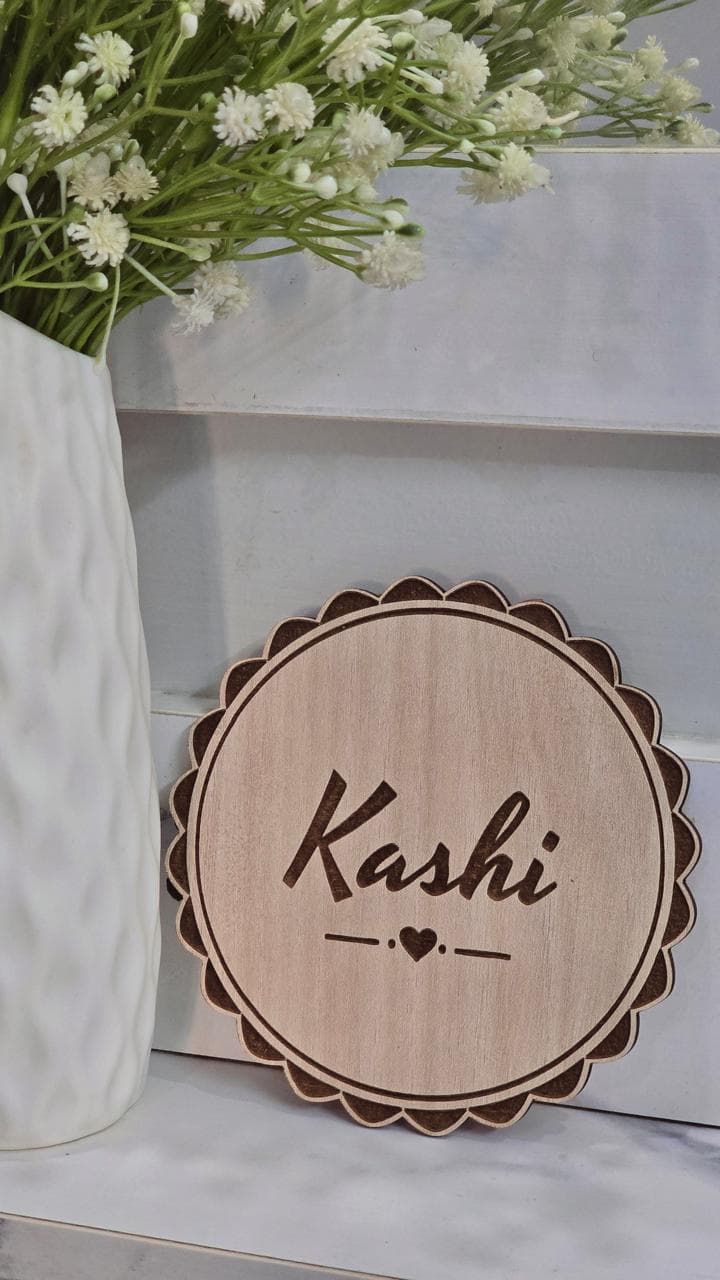 Scalloped wooden name plaque with Kashi engraved, beside white flowers